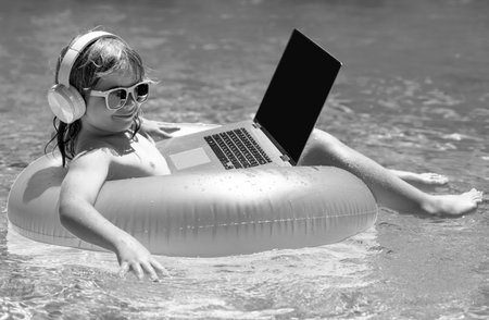 Freelance work concept. Child working on laptop computer at poolside swimming pool. Summer online technology. Traveler relaxing on tropical sea beach in summer holidays vacation. Business travel.の写真素材