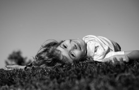 Cheerful boy laying on the green grass. Happy child playing in green spring field against sky background. Freedom and imagination concept.の写真素材