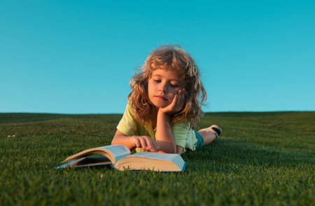 Cute kid reading book on green grass. Schoolboy with a book having a rest outdoor.の写真素材