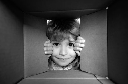 Child open paper cardboard box. Kid boy unpacking and opening carton box looking inside with surprise face. Parcels and delivery.の写真素材