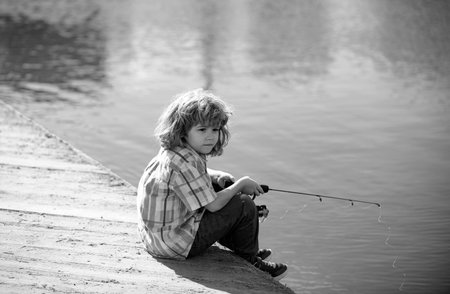 Young kid fisher. Child fishing at river bank, summer outdoor leisure activity. Little boy angling at river bank with rod.の写真素材