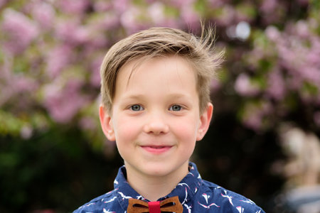 Fashion kid boy in shirt and bow tie. Portrait of kid in spring park outdoors. Close-up face child...