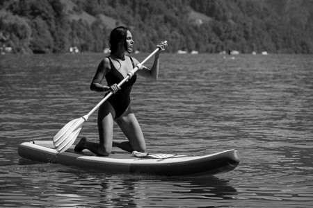 Beautiful young woman relaxing on paddle board in the summer lake or sea water. Luxury summer...