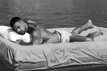 Mattresses, Comfort sleep, good dreams concept. Sexy man floating on the Bed with blanket. Summer relaxation concept. Calmness and relax in summer beach. Ideal fit body. Muscular Italian man on beach.の写真素材
