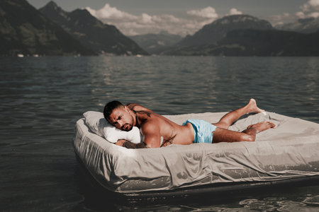 Summer Travel vacation holiday. Relax man, freedom, calm and carefree on summer concept. Muscular man lying on cozy Mattresses, sleep, good dreams concept. Sexy man floating on the Bed with blanket.の写真素材