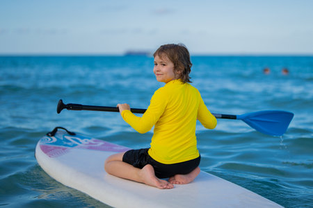 Boy swimming on stand up paddle board. Water sports, active lifestyle. Kid paddling on a paddleboard in the ocean. Child Paddle boarder. Summer Water sport, SUP surfing. Summer beach vacation.の写真素材