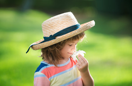 Portrait of a cute child boy in straw hat smelling plumeria flower. Close up caucasian kids face. Closeup head of funny kid.の写真素材