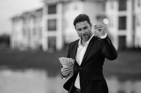 Realtor with money dollars and house keys against the background on new apartment home. Realtor in suit demonstrating keys and cash, outdoor portrait. Realtor offering new home. Property concept.の写真素材