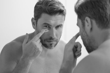 Sexy sensual man with perfect skin touch face after shaving. Skin care healthcare cosmetic procedures concept. Close up man looking in mirror, sensitive skin, cosmetology treatment. Skin care.の写真素材