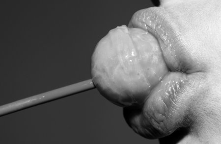 Lollipop in the mouth, close-up. Beautiful girl mouth with lolli pop. Oral sex blow job concept. Glossy red woman lips with tongue. Mouth lick suck chupa chups.の写真素材