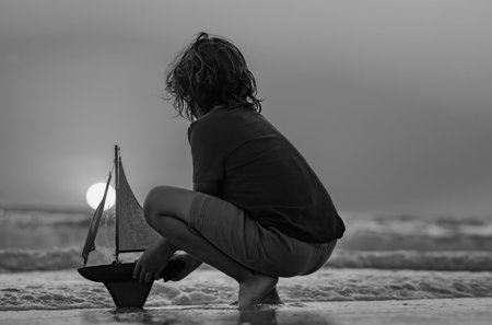 Kids travel concept. Kid playing with toy sailing boat on summer sea background. Travel and summer vacations. Child playing with toy boat in water on the beach. Outdoor summer activities for kids.の写真素材