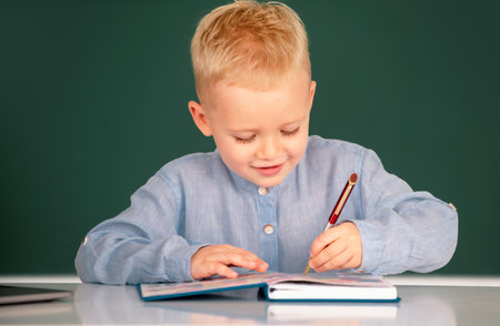 Little student child studying in classroom at elementary school. Pupil near chalkboard during lesson at primary school, close up portrait.の写真素材