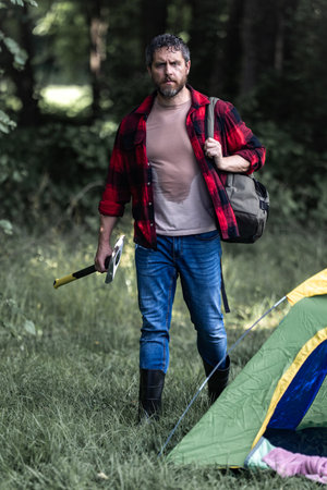 Bearded lumberjack. Bearded man in checkered shirt and ax in forest. Serious lumberjack holding axe and looking away outdoors. Lumberjack worker.の写真素材