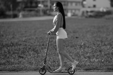 Girl lifestyle. Cool young woman standing on funny scooter. Girl riding scooter. A girl rides a scooter in shorts. Summer sports and outdoor active. Girl riding an scooter in summer street.の写真素材