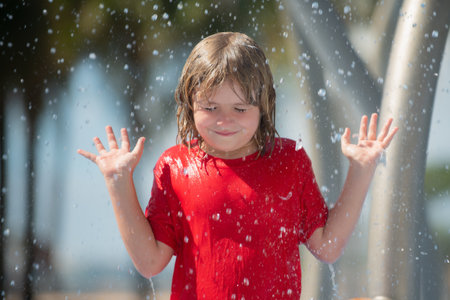 Summer kid enjoying splashes in summer day. Kid splashing in outdoor kids Public shower. Happy kid playing in water fountains. Kid having fun with fountain during summer time. Hot summer day.の写真素材