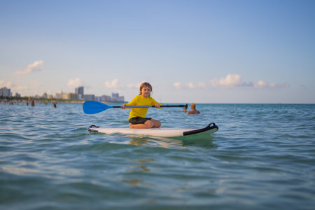 Kid riding on a paddle board. Summer holidays. Kid paddle surf surfer little blonde boy in summer...