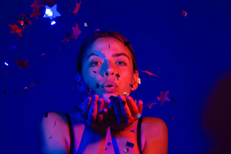 Woman blowing confetti. Beautiful young woman on birthday, valentines day. Woman blow sparkles on birthday. Woman celebrating birthday. Happy valentines day. Birthday party.の写真素材