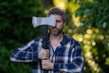 Lumberjack bearded man in checkered shirt with ax on green nature. Man with axe in forest. Woodsman....