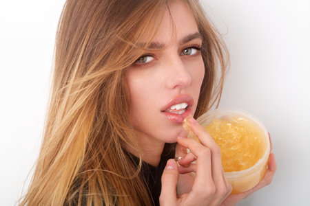 Facial treatment. Woman lips balm. Girl enjoying a facial treatment with a lips cream. Lips skin care. Young woman hold cream jar. Portrait of beauty woman with cream for healthy lips. Gold cosmetics.の写真素材