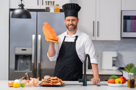 Chef cook in cook apron and chef hat cooking raw fish salmon fillet in the kitchen. Restaurant menu...