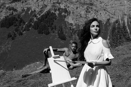 Artist couple in love drawing outdoor. Lovers Painting art. Friends artists draw pictures in alps mountain. Artist paints a picture on canvas.の写真素材