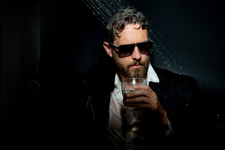 Drunk business man. Disheveled man in suit in bathroom after night party. Man drinking a whiskey after party in night club. Alcohol and drugs concept. Stressed business man under shower.の写真素材