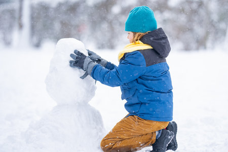 Happy Kid make snowballs for snowman in winter. Kid play in snow. Active winter outdoor games. Boy having fun playing with snow. Winter outdoors leisure for kids. Child play on sunny winter day.の写真素材