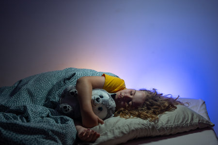 Child sleeping in a bed. Cute kid sleep. Kids pillow and blanket for sleeping. Little boy sleeps. Adorable kid sleeps in bed. Sleeping child. Kid sleeping in dark bedroom.の写真素材