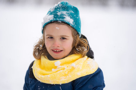 Kids face in snow. Happy Child playing with Snowball. Child in winter clothes play with snow. Winter...