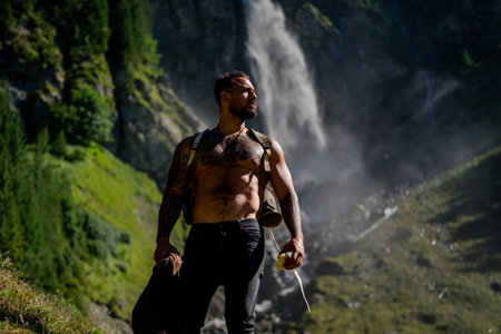 Man hiker on summer vacation. Tourist hiker with muscular torso. Strong Hispanic Tourist Hiker outside. Hiker walking near the waterfall. Traveling on nature. Carefree hiking. Hiking on mountain.の写真素材