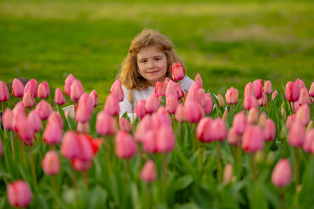 Tender Spring. Child play outdoors in a beautiful spring garden. Kid face in tulip flowers. Adorable little kid in blooming tulips garden on beautiful spring day. Cute little kid with tulips in park.の写真素材