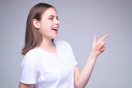 Young woman pointing copy space. The point. Studio portrait of Girl looking at camera and pointing away on gray isolated background. Finger point gestures.の写真素材