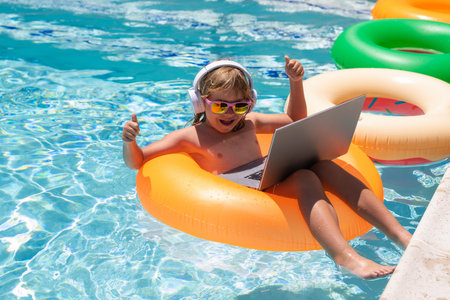 Child working on laptop computer at poolside swimming pool. Summer online technology. Traveler...
