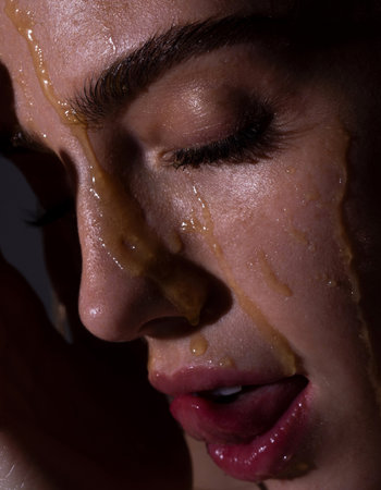 Sensual young woman face with honey drop close up. Sexy model with honey drip on face. Honey mask.の写真素材