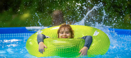 Kid playing in kids pool at home. Kids swim and splash in pool in garden backyard. Kids boy swim in inflatable circle pool on summer sunny day outdoors on home yard. Kids swimming pool at home.の写真素材