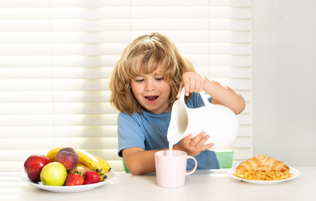 Kid pouring whole cows milk. Kid preteen boy in the kitchen at the table eating vegetable and fruits during the dinner lunch. Healthy food, vegetable dish for children.の写真素材