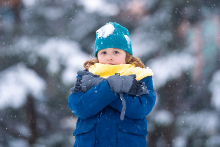 Happy teen child playing with snow during snowfall. Child in winter clothes, hat, gloves and scarf. Winter children play with snow. Happy winter holidays. Kid play with snowball. Winter kids portrait.の写真素材
