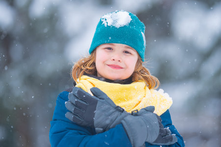 Child playing with snow during snowfall. Snowball fight Child in winter clothes throw snowball. Winter children play with snow. Kid play with snowball. Winter kids face. Boy play snowball.の写真素材