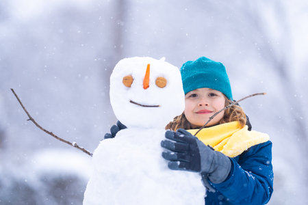 Excited Kid in winter park on a snowy cold winter day. Cute child playing with snow in winter. Portrait of funny child play with snowman. Winter activities Christmas. Kid building snowman in park.の写真素材