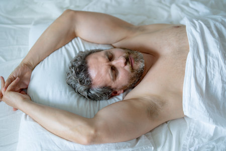 Adult man sleeps in white bed. Handsome shirtless man sleeping in bed at bedroom. Hispanic mature man sleeping at home at morning. Good sleep. Man sleeping in bed. People bedtime, rest sleep concept.の写真素材