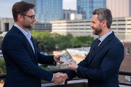 Businessmen shaking hands and receiving banknote. Businessman giving money outdoor. Receiving money. Bills money,finance staff counting money, finance, saving, banking, and people concept.の写真素材