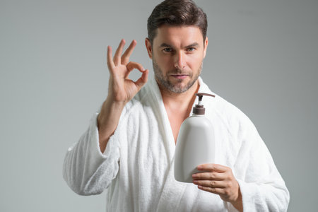 Cosmetic products. Beauty man presentation cosmetic bottle isolated on gray studio background. Natural cosmetics cream, spa beauty products. Man advertising cosmetic. Male beauty model.の写真素材