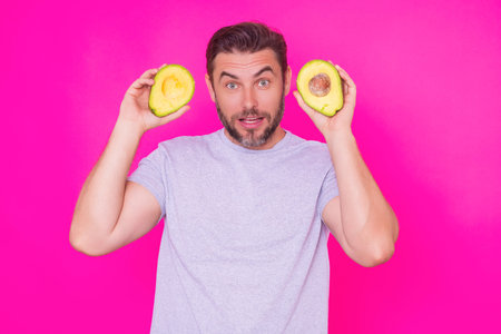 Funny surprised Man hold half of fresh avocado isolated on pink background, studio portrait. The...