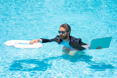 Helping businessman. Businessman in suit hold laptop and lifebuoy in sea beach water. Rescue businessman. Helping businessman. Save and help business.の写真素材