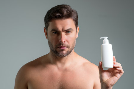 Male model hold bottle with dispenser pump for liquid soap, gel or foam. Facial treatment. Beauty portrait of sexy man cosmetics products, beauty and spa. Skincare. Perfect skin, morning routine.の写真素材
