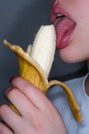 A woman is eating a peeled banana. Close-up of female mouth eating banana. Lady biting banana. Red lips. Girl sucking and licking.の写真素材