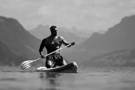 Sexy man with paddle board. Man paddling on paddleboard. Muscular strong Hispanic man on sup board paddle surfing. SUP surfing in summer vacation in lake. Strong muscular wet body. Bare naked torso.の写真素材