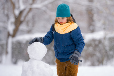 Happy Kid make snowballs for snowman in winter. Kid play in snow. Active winter outdoor games. Boy having fun playing with snow. Winter outdoors leisure for kids. Child play on sunny winter day.の写真素材