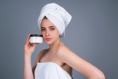 Skin care. Beauty portrait of a beautiful woman applying face cream isolated on studio background. Young spa model uses body care cream. Facial cream, moisturizing lifting nourishing creme.の写真素材