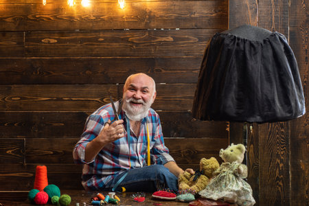 Happy senior man knit. Old man knitting at home. Elderly men making clothes for toys with needles and wool yarn. Retirement home. Senior man knitting with woolen yarn at home. Pension and retirement.の写真素材